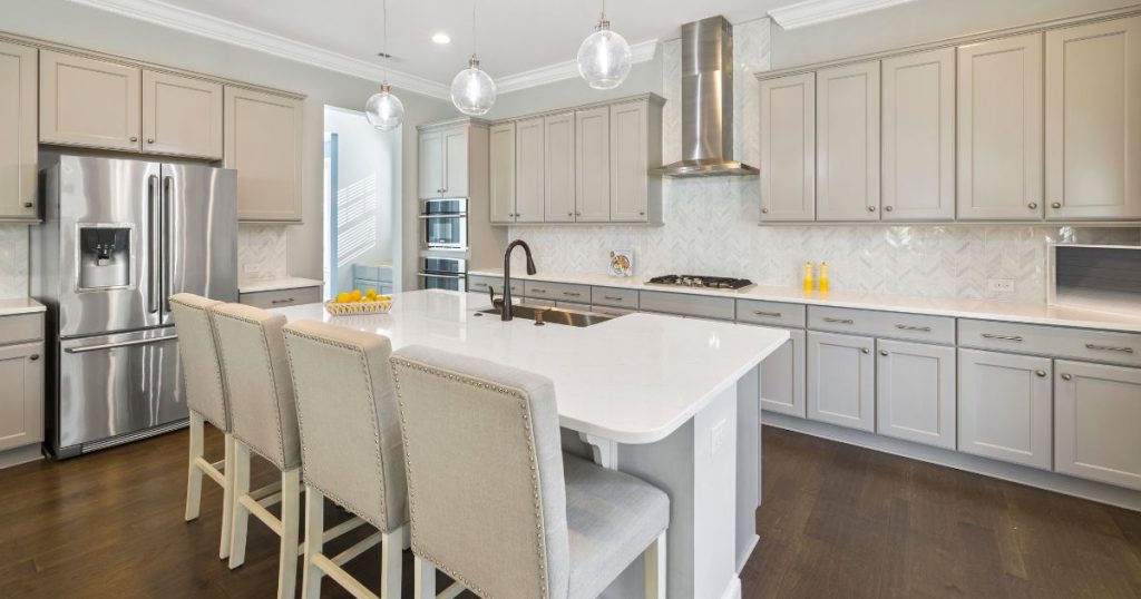 neutral colored kitchen with four barstool chairs at the island and yellow accents